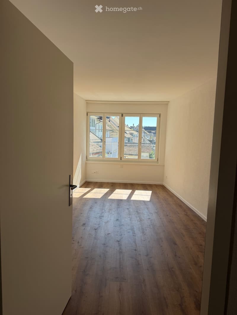 Empty room with wooden flooring, large windows, and neutral-colored walls.