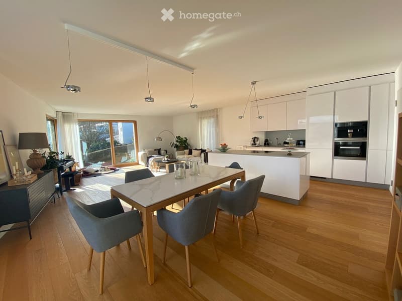 Open-plan living and dining area with modern furniture, a kitchen area, and large windows letting in natural light.