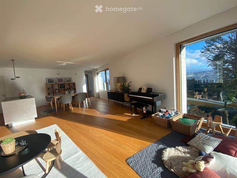 Bright, open living space with wooden flooring, large windows offering a scenic view, and a mix of seating and dining areas.