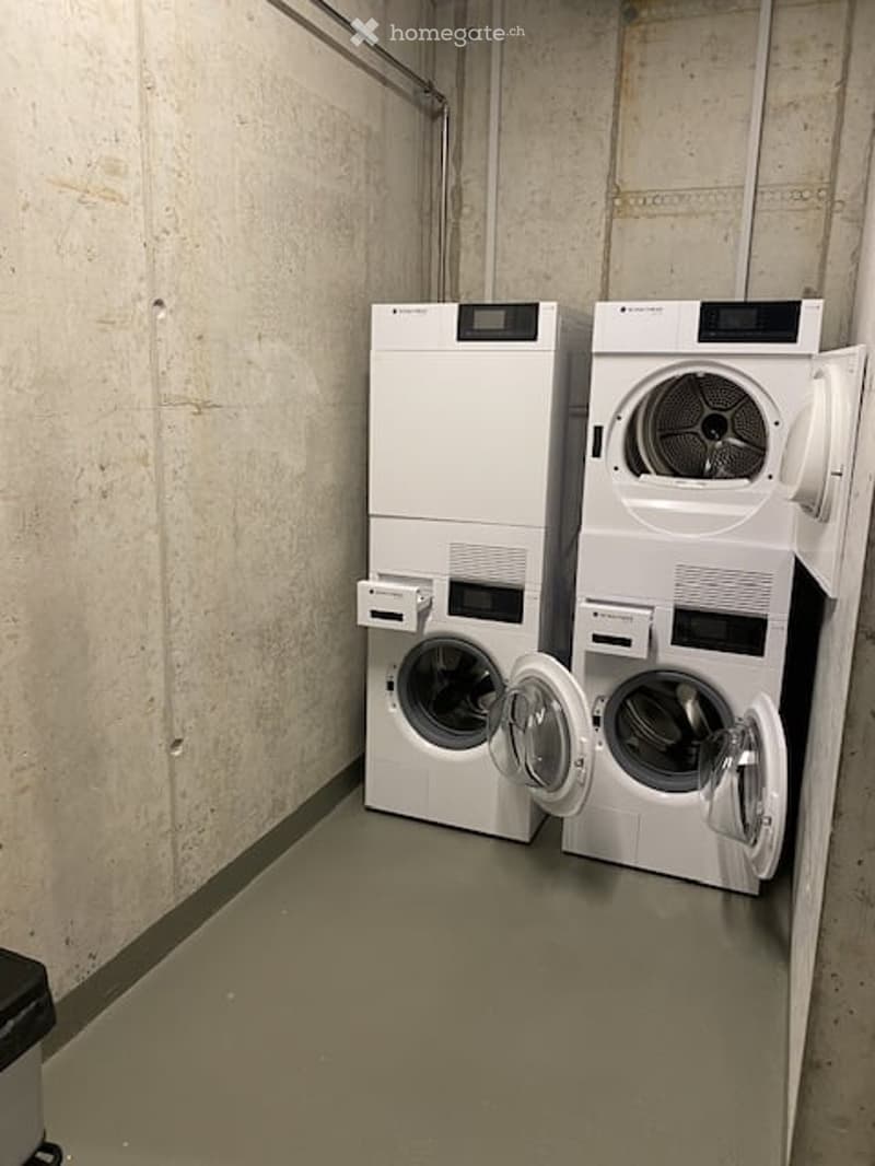 A small, clean laundry room with a white washing machine and dryer side by side, both with open doors.