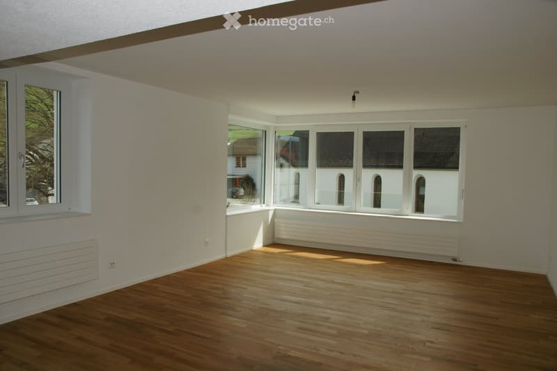 Empty room with wooden flooring, large windows, and radiators along the walls. No furniture or personal items are present.