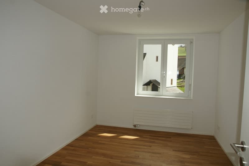Empty room with wooden flooring, white walls, a large window, and a radiator below the window.