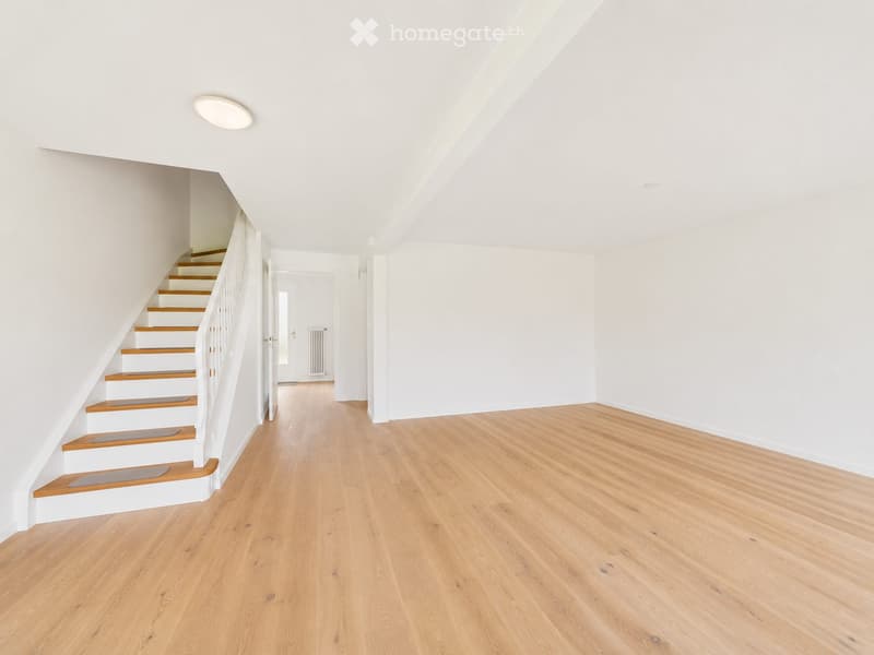 Empty room with light wooden flooring, white walls, and a staircase leading upwards. The space is clean and minimalistic with no furniture or decorations.