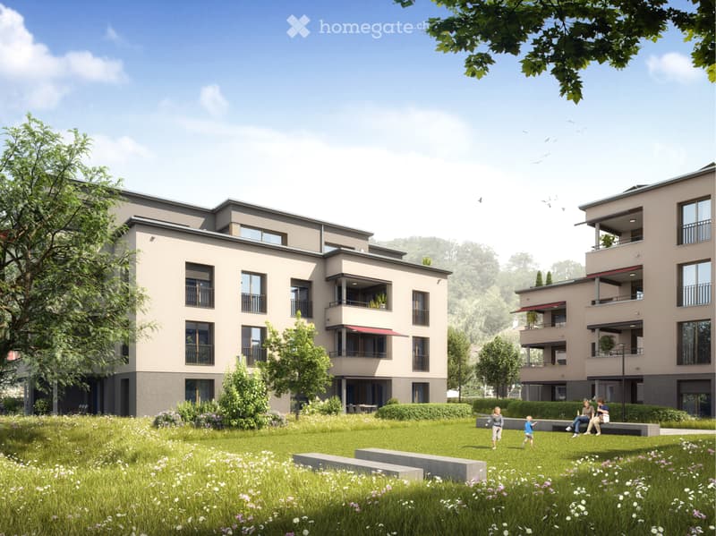 Modern two-story residential building with balconies, surrounded by a green lawn and trees. The building features large windows and a contemporary design.