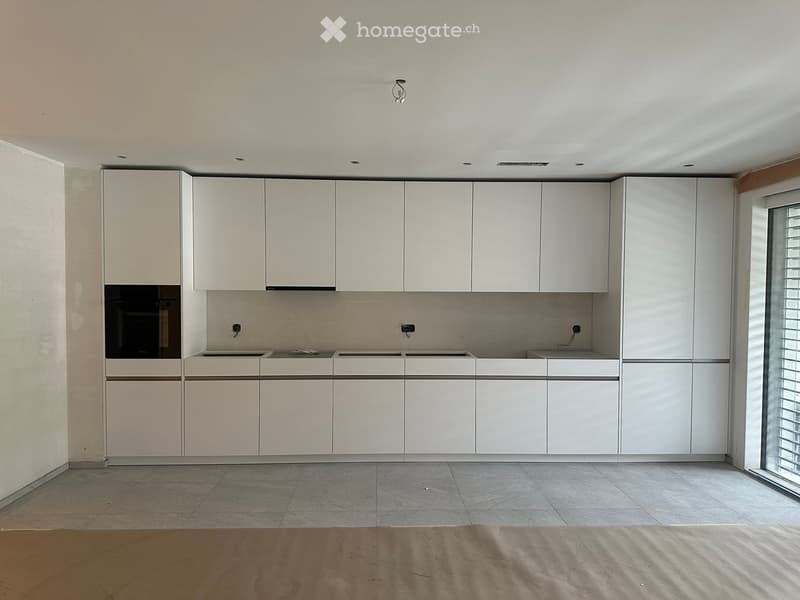 Empty kitchen with white cabinets, a sink, and a tiled floor. No appliances or furniture are present.