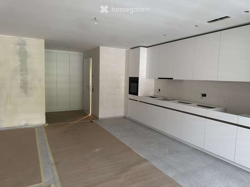 Empty kitchen with white cabinets, stainless steel sink, and oven. Bare walls and floor, no furniture or appliances installed.