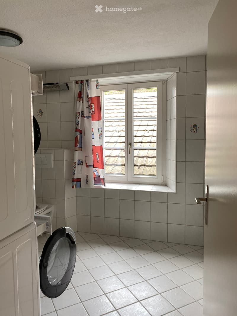 Bathroom with tiled walls and floor, a toilet, a shower curtain, and a window with a view of a roof.