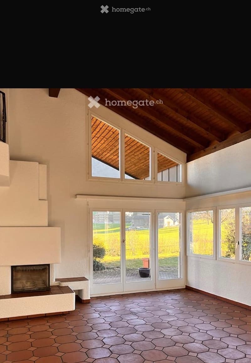 Bright living room with a fireplace, large windows, and a bench, featuring a hexagonal tile floor and wooden ceiling.