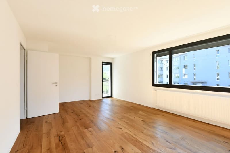 Empty room with wooden flooring, white walls, large windows, and a door leading to a balcony.