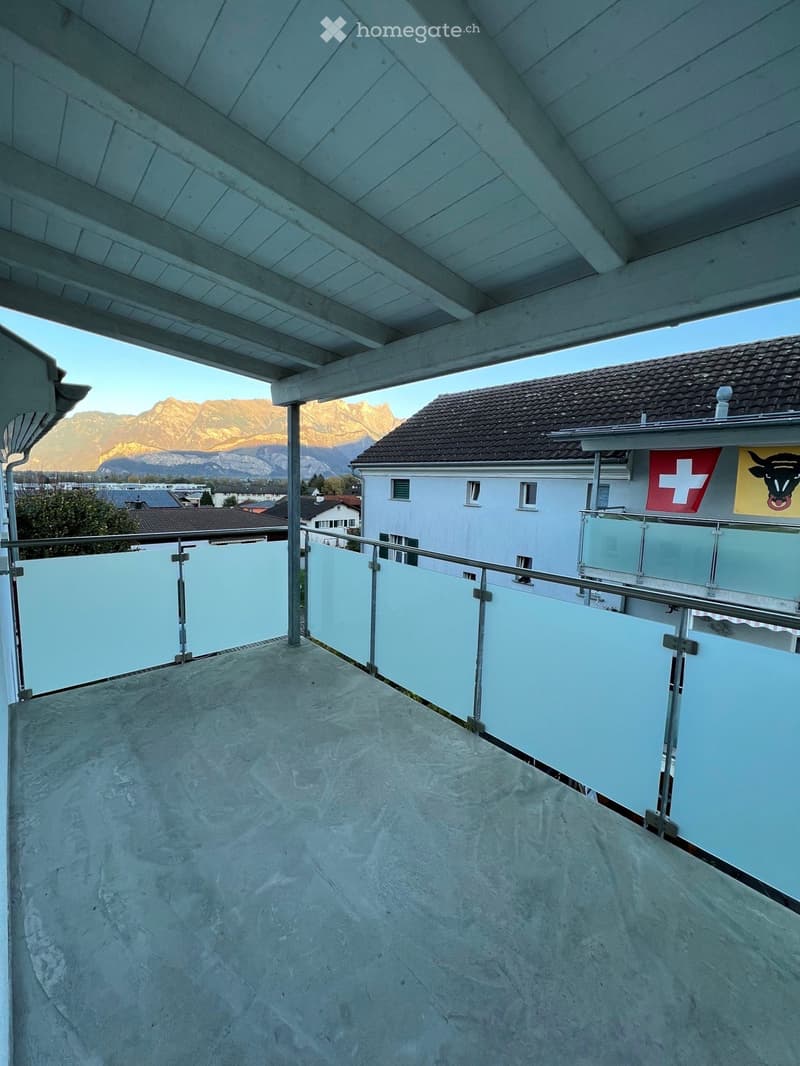 Balcony with a modern glass railing, concrete floor, and a view of mountains in the background.