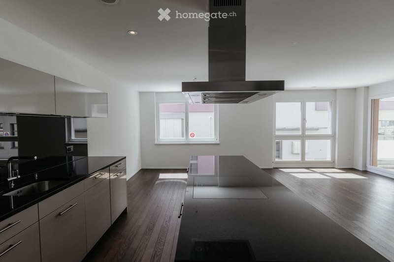 Modern kitchen with wooden flooring, stainless steel cabinets, a central island, and a large range hood. The space is bright with multiple windows and a sleek, minimalist design.