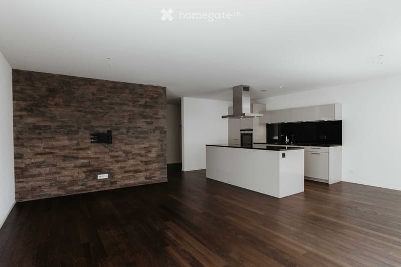Modern kitchen with dark wooden flooring, white cabinetry, a central island, and a range hood. The backsplash is black, and there is a wooden accent wall on one side.