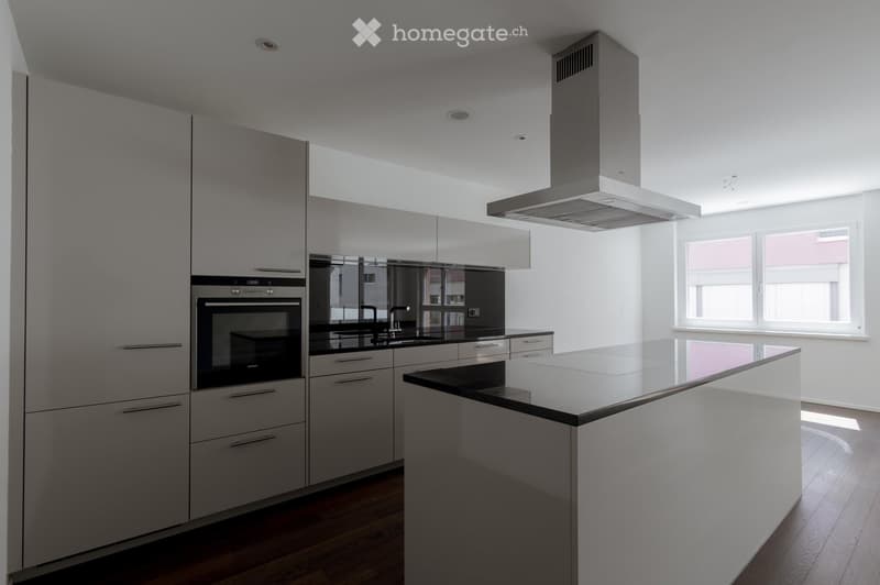 Modern kitchen with grey cabinets, stainless steel appliances, island, and large windows.