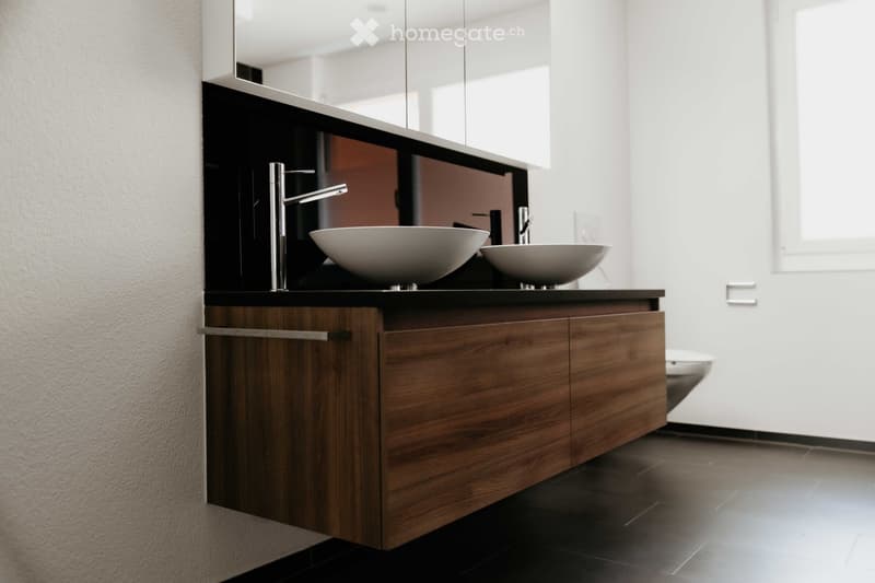 Modern bathroom with a dark wooden vanity, two white sinks, sleek chrome faucets, and a large mirror above.