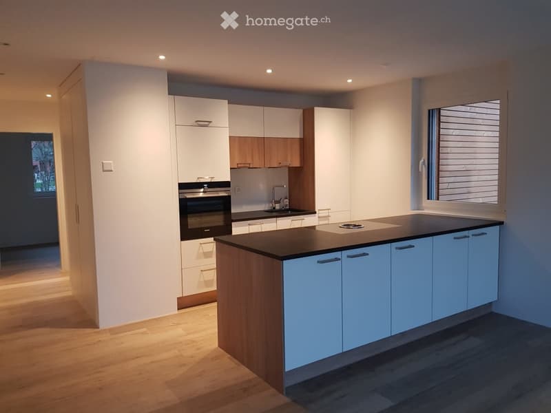 Modern kitchen with white and light blue cabinets, a central island with a black countertop, an oven, and a sink with a faucet.