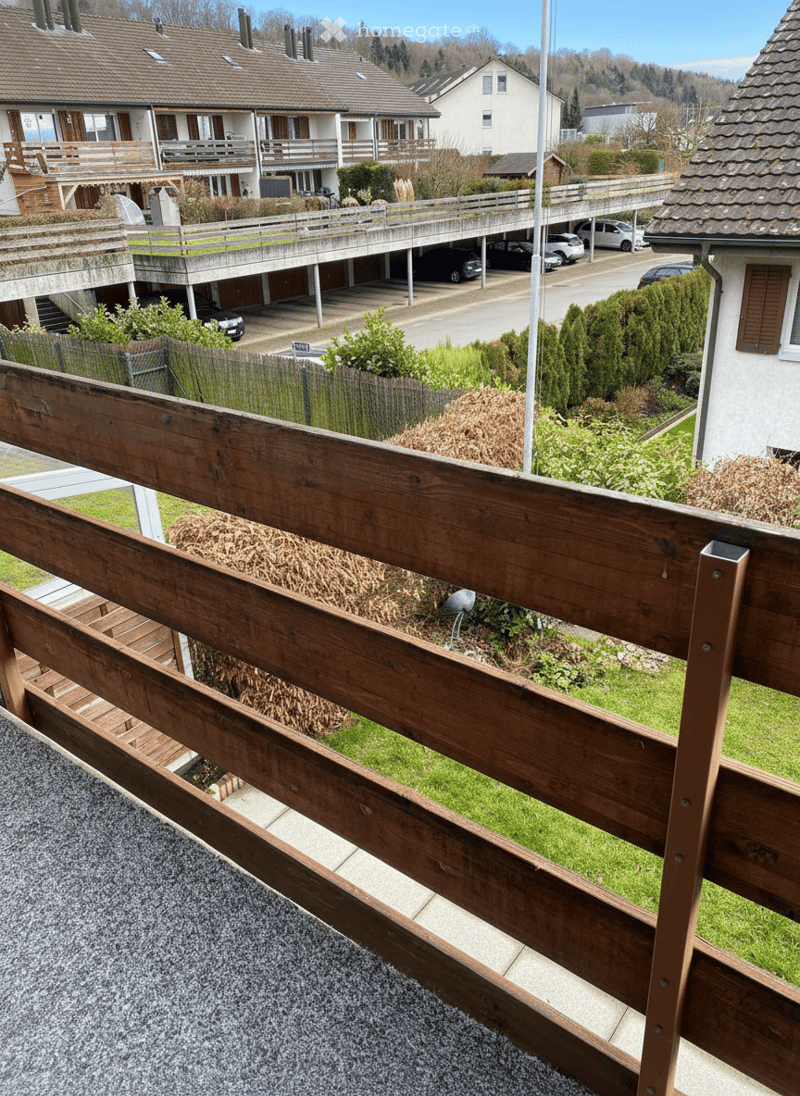 Wooden railing, balcony, apartment building, garage with cars, road, bushes, dry plants