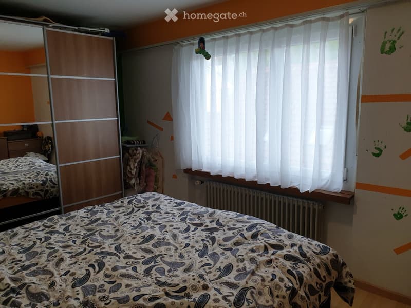 Bedroom with a large bed, patterned bedspread, sliding wardrobe, mirror, and radiator under the window.