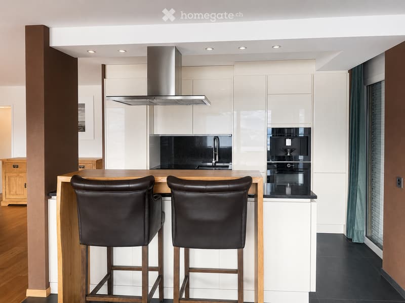 Modern kitchen with white cabinets, a wooden island, two black bar stools, a stainless steel range hood, and built-in appliances.