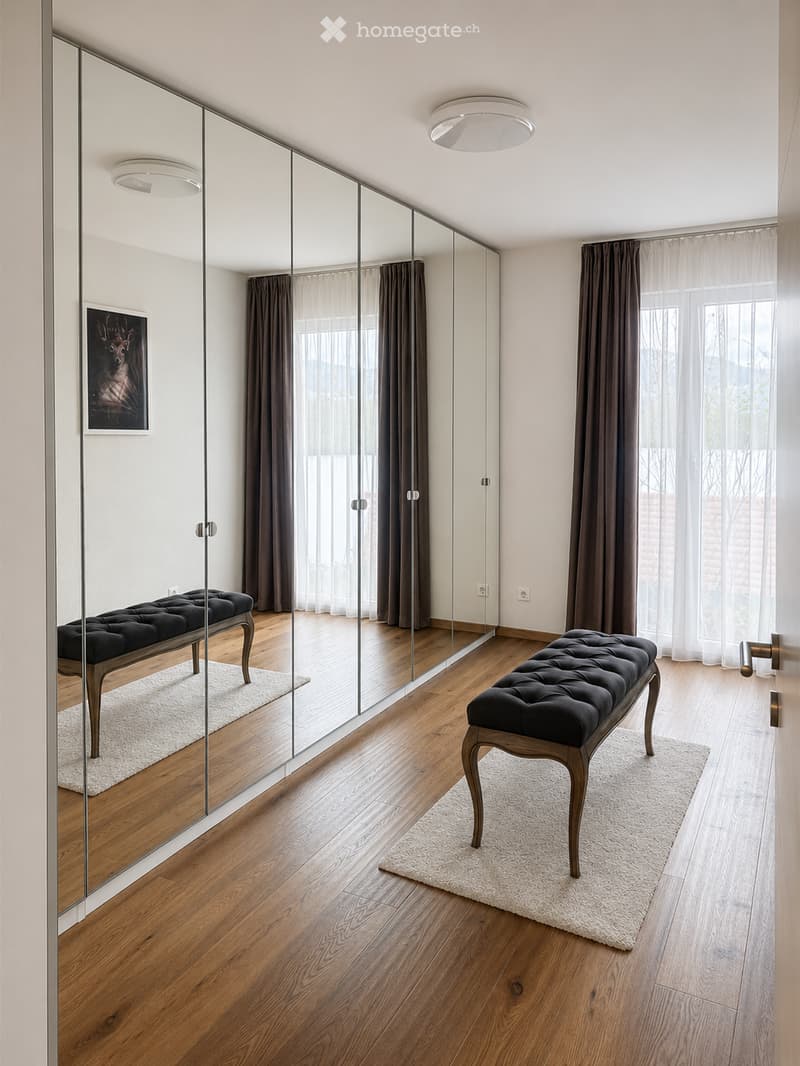 Modern hallway with wooden flooring, large mirrored wall, two black upholstered benches, and a framed picture on the wall.