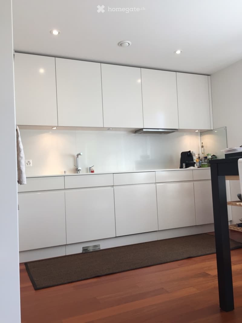 Modern kitchen with white cabinets, a stainless steel sink, and a wooden floor. A small black table is visible in the foreground.