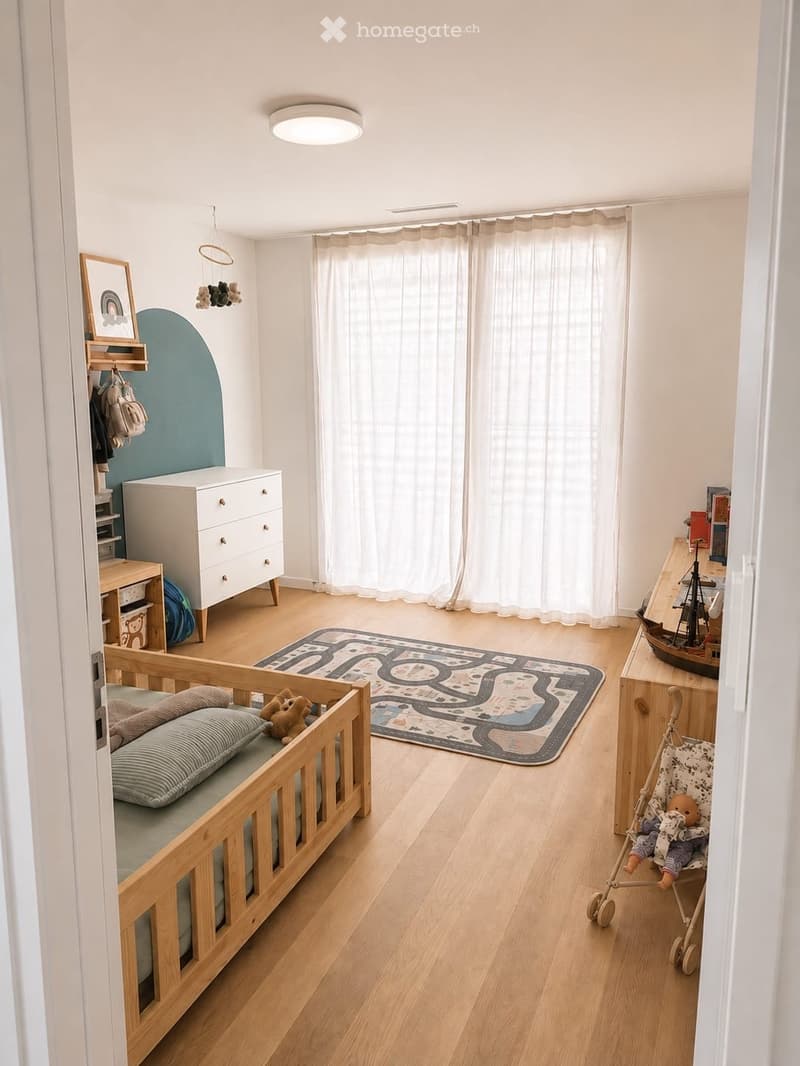 A well-lit children's bedroom with a crib, toy car rug, toy ship, and a toy stroller. The room features a wooden floor, white walls, and a large window with white curtains.