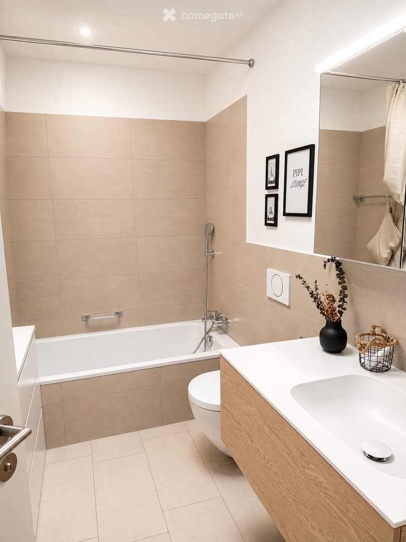 Modern bathroom with a bathtub, toilet, sink, large mirror, and decorative vase on the counter.