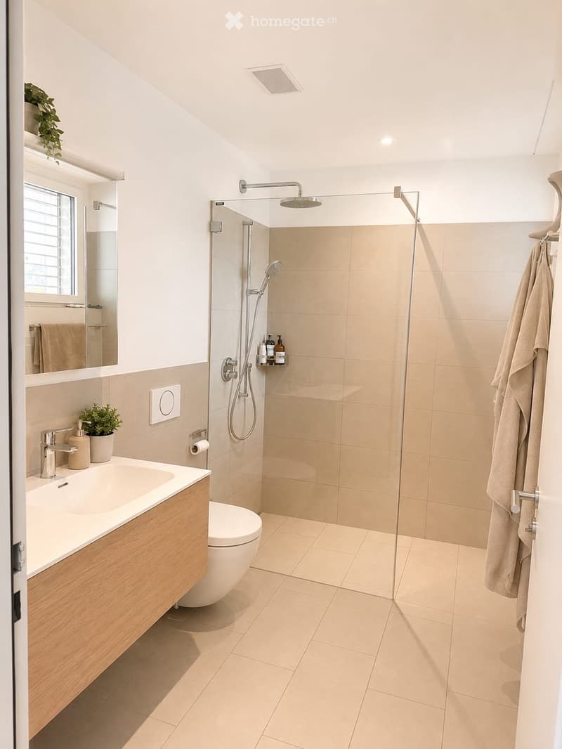 Modern bathroom with a large shower, sink, toilet, and a small window. Features include a glass shower enclosure, a wooden vanity, and a potted plant on the windowsill.