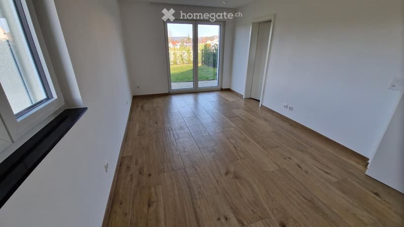 Empty room with wooden flooring, large windows, and a sliding glass door leading to an outdoor area.