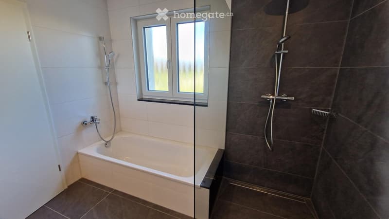 Modern bathroom with a bathtub, separate shower area, and a window above the tub. Features tiled walls and floor, with a glass shower enclosure.
