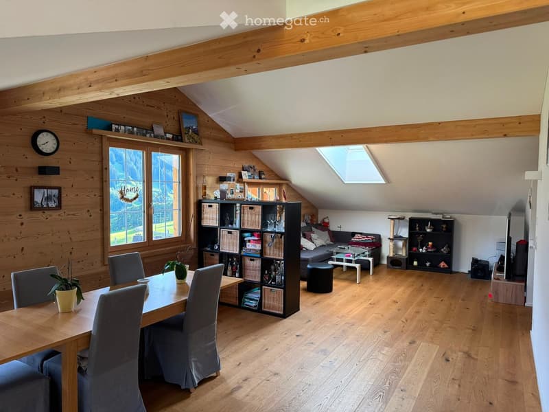 Bright, wooden-floored room with exposed wooden beams, large windows, skylight, dining table with chairs, sofa, cat tree, shelves, and decorative items.
