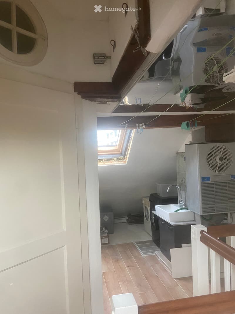Bathroom with a sink, faucet, washing machine, air conditioner, and fan. The room has wooden flooring and exposed wooden beams on the ceiling.
