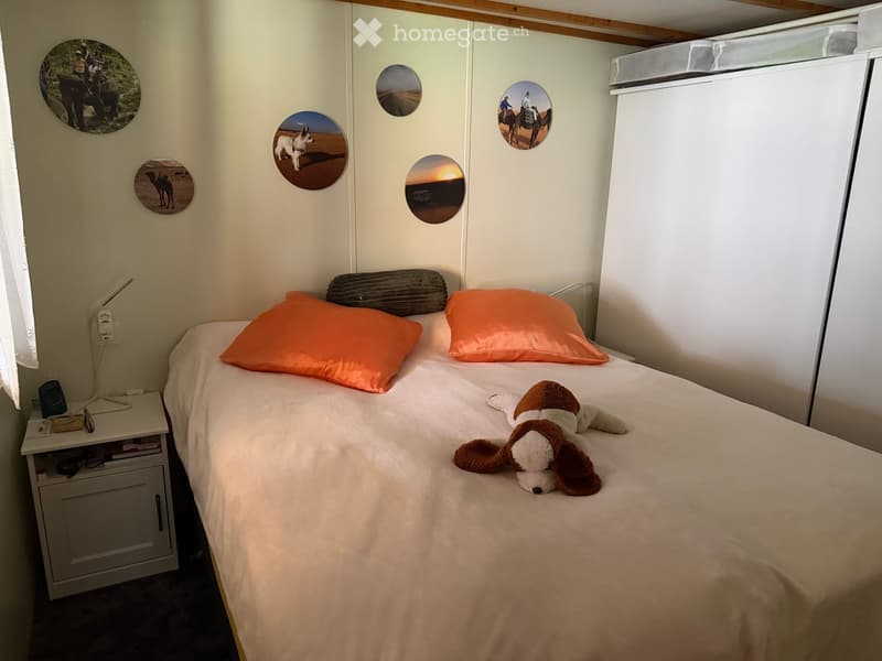 Cozy bedroom with a single bed, two orange pillows, a stuffed dog toy, a nightstand with a lamp, and decorative wall stickers.