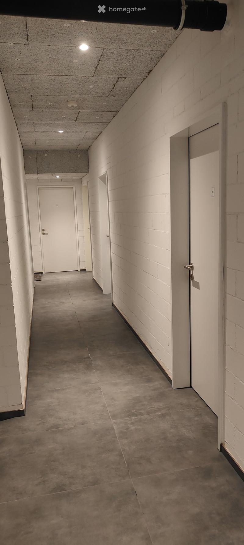 Empty hallway with concrete floors, white brick walls, and white doors at both ends.