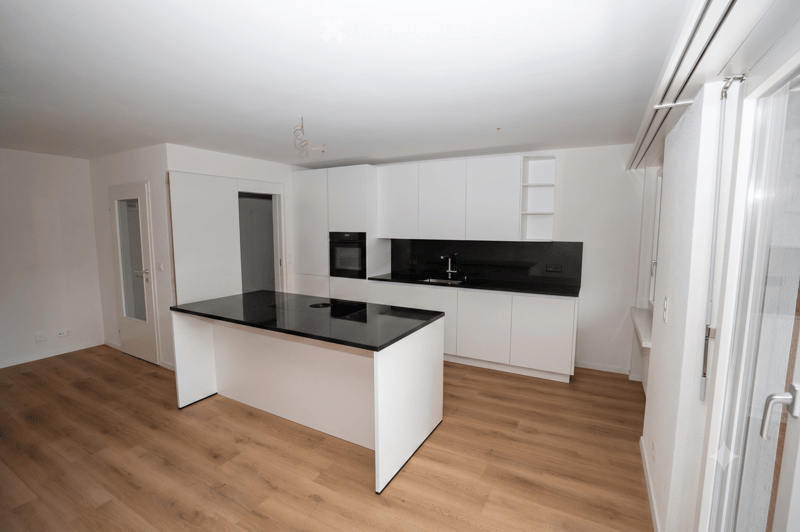 Modern kitchen with white cabinets, black countertops, and wooden flooring.