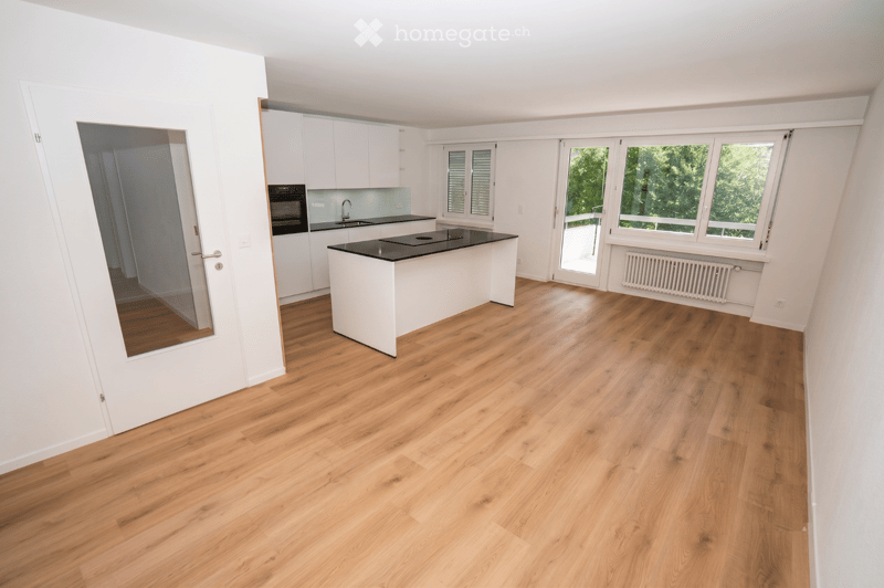 Modern kitchen with light wooden flooring, white cabinetry, a central island with black countertop, and built-in appliances including an oven and sink.
