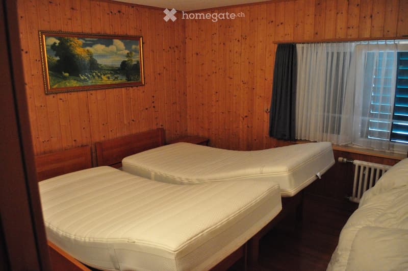 Cozy bedroom with wooden walls, two single beds, a nightstand, a radiator, and a framed painting on the wall.