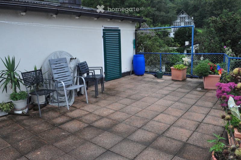 Balcony with tiled floor, several chairs, potted plants, and a covered object.