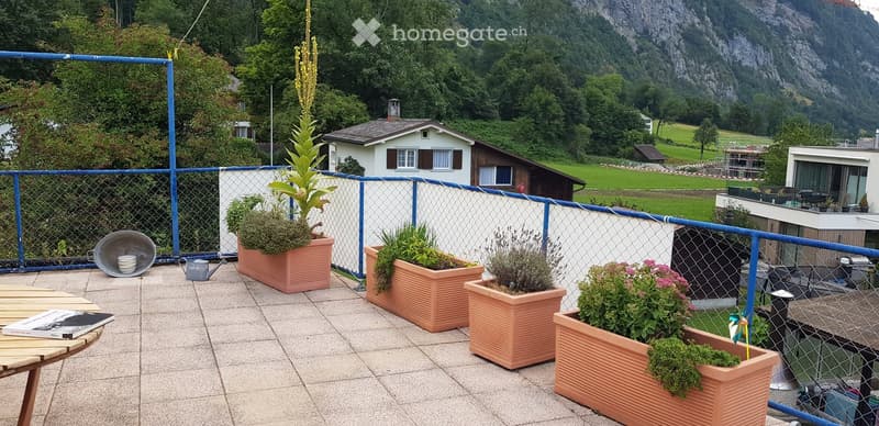 Balcony with potted plants, a small table, and a scenic mountain view in the background.