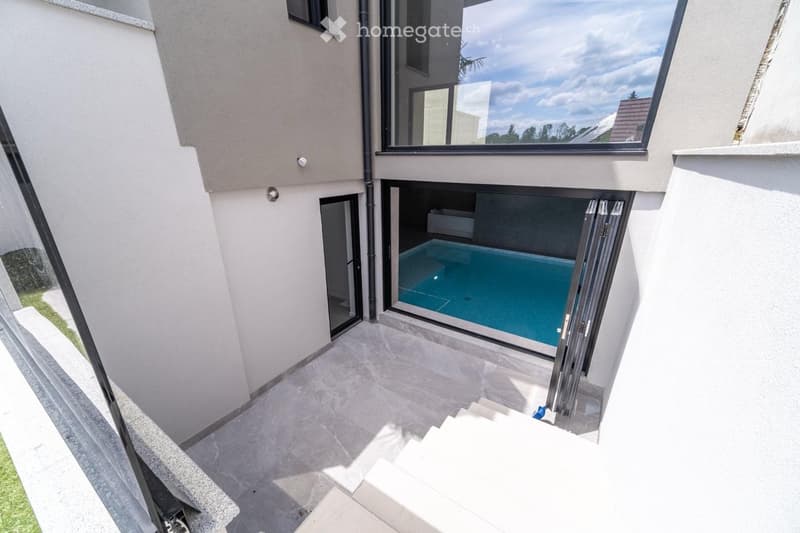 Modern outdoor area with a swimming pool, large windows, and a staircase leading up.