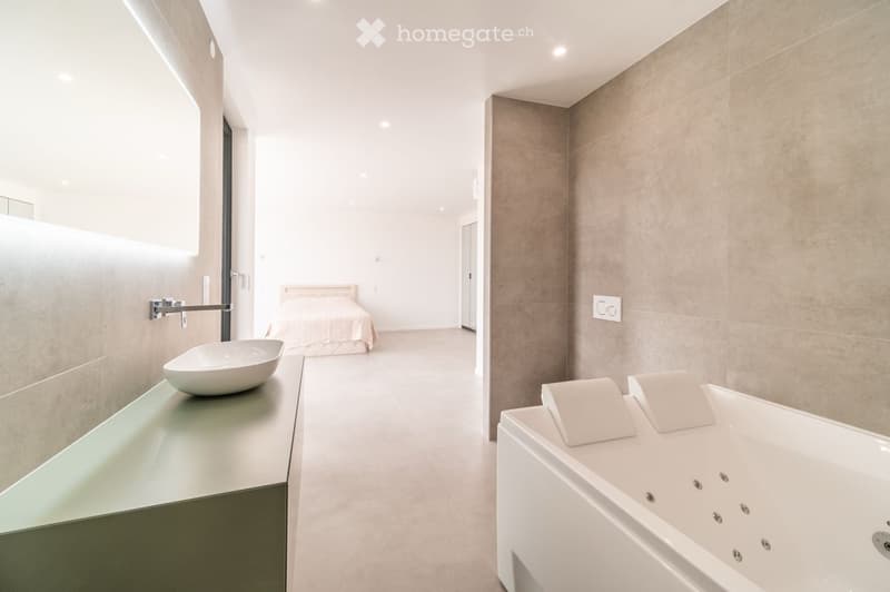 Modern bathroom with a sleek white sink, bathtub, and glass shower enclosure. The space features light-colored tiles and a minimalist design.