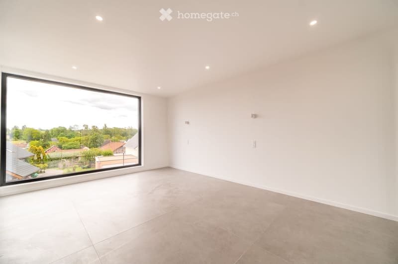 Empty room with white walls, tiled floor, large window offering a view of the neighborhood, and recessed ceiling lights.