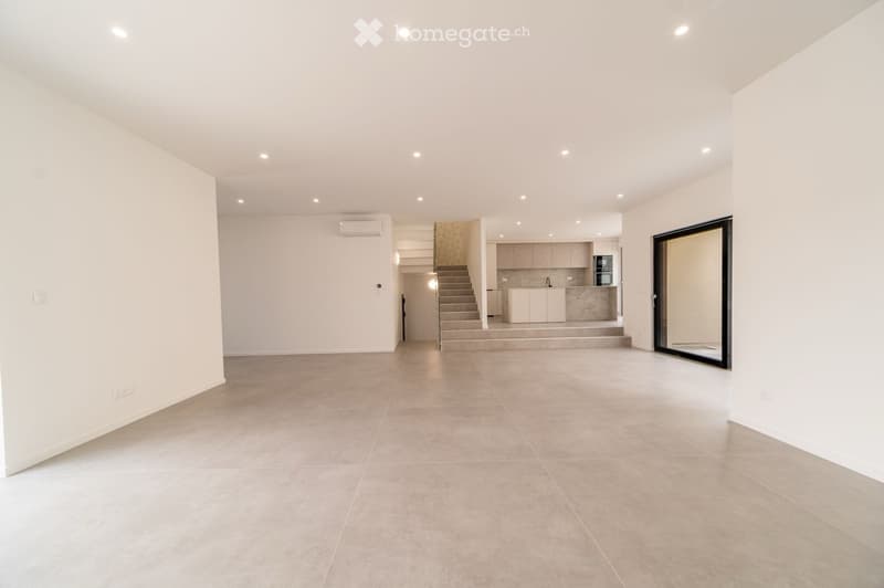 Empty living space with tiled floor, white walls, recessed lighting, and an open doorway leading to a staircase and kitchen area.