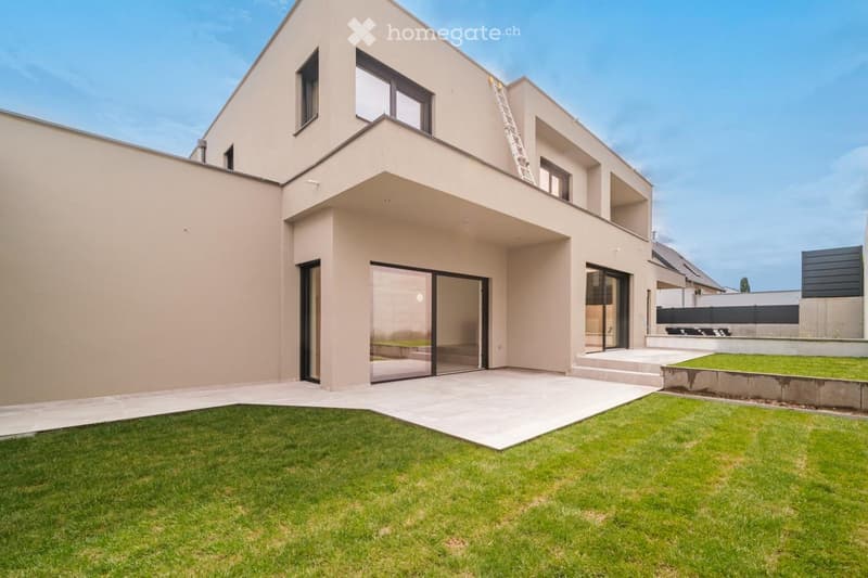 Modern two-story house with beige exterior, large windows, and a spacious front yard with neatly trimmed grass and a concrete pathway leading to the entrance.