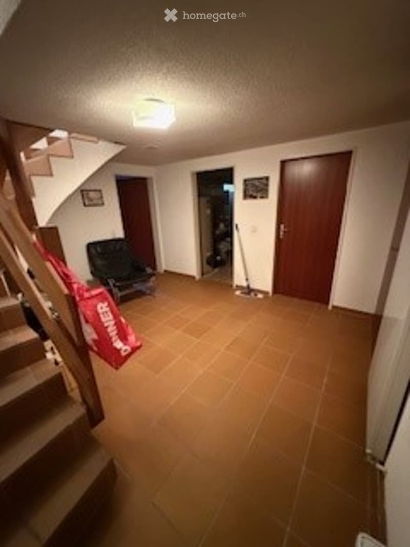 Empty room with tiled floor, white walls, staircase leading up, and a single chair near the wall.