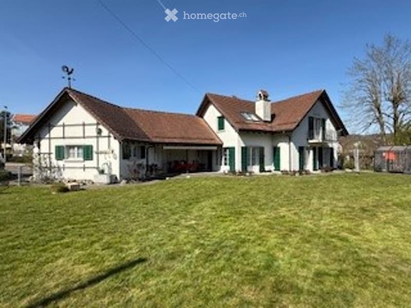 A two-story house with a white exterior and green shutters, featuring a red-tiled roof and a well-maintained lawn in front.