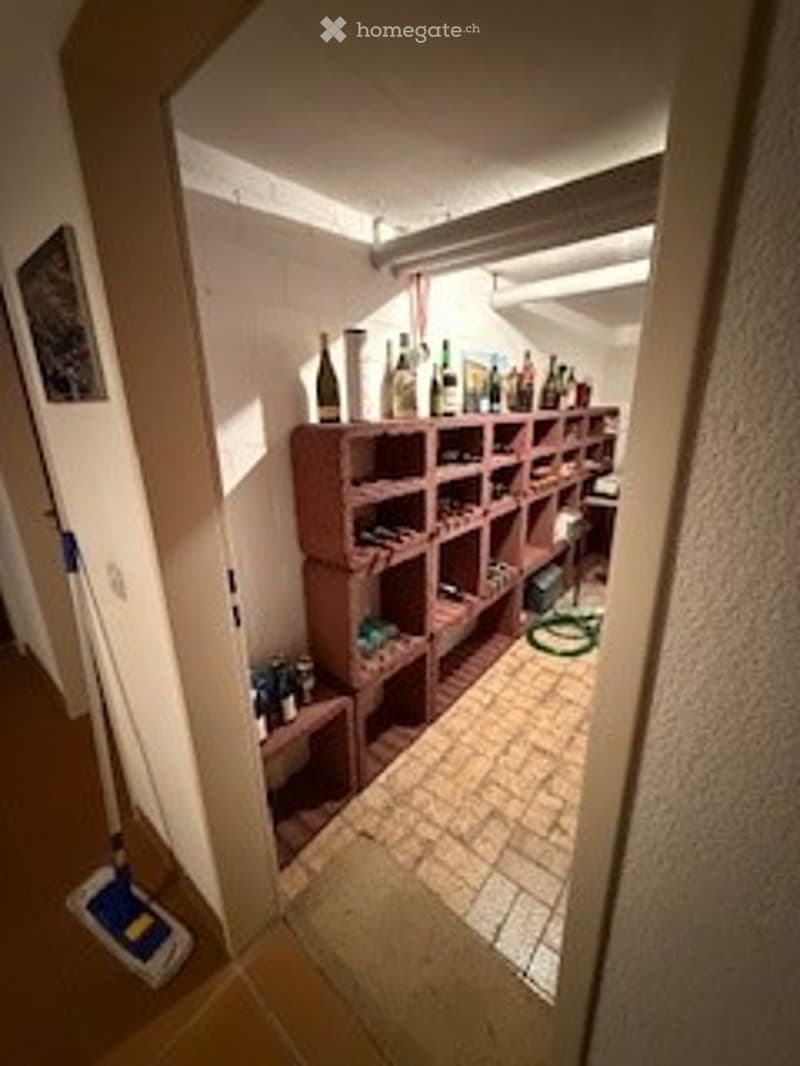 Empty storage room with wooden shelving units, tiled floor, and a broom in the adjacent hallway.