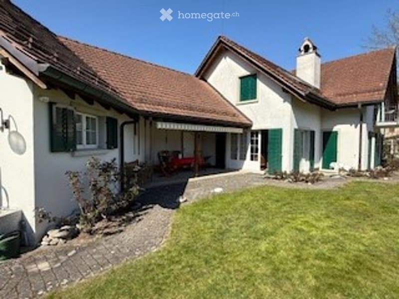 Two-story white house with green shutters, red-tiled roof, and a well-maintained lawn.