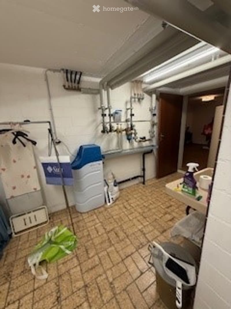 Utility room with tiled floor, sink, fridge, and cleaning supplies.