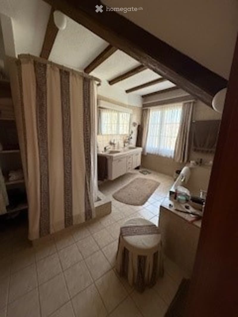 Bathroom with exposed wooden beams, tiled floor, bathtub, sink, small stool, and a rug.