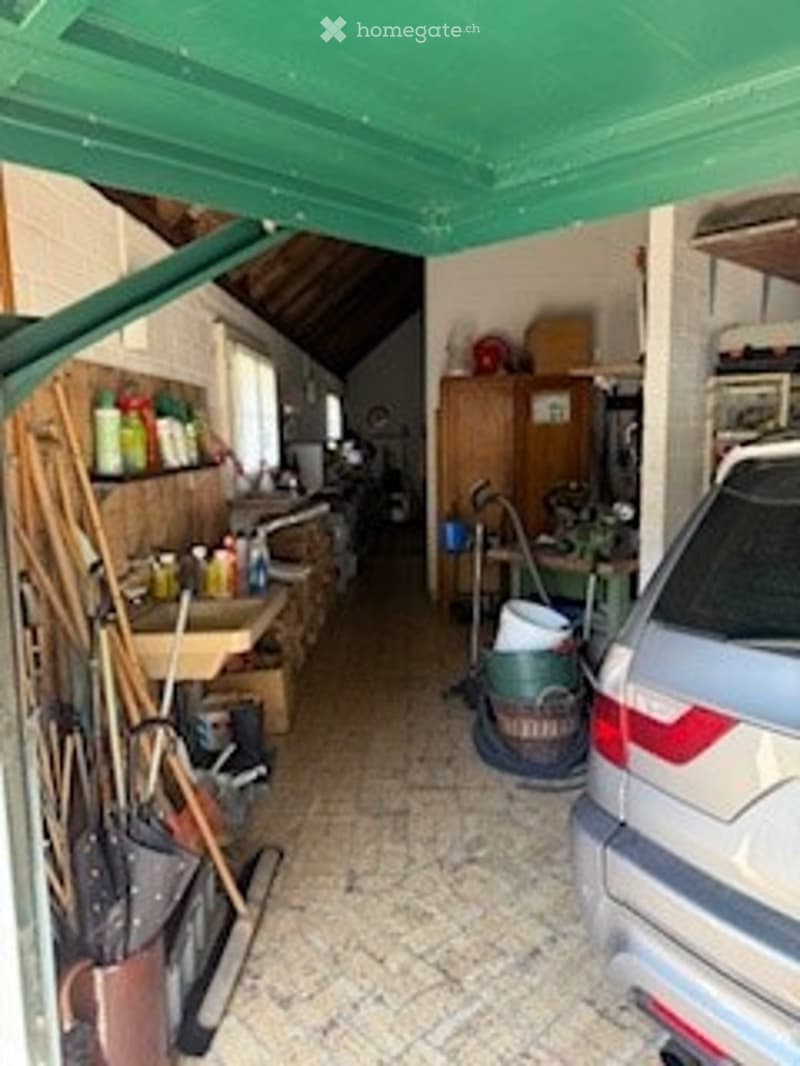 Garage with tiled floor, wooden ceiling, tools, a table, a cabinet, and a parked car.